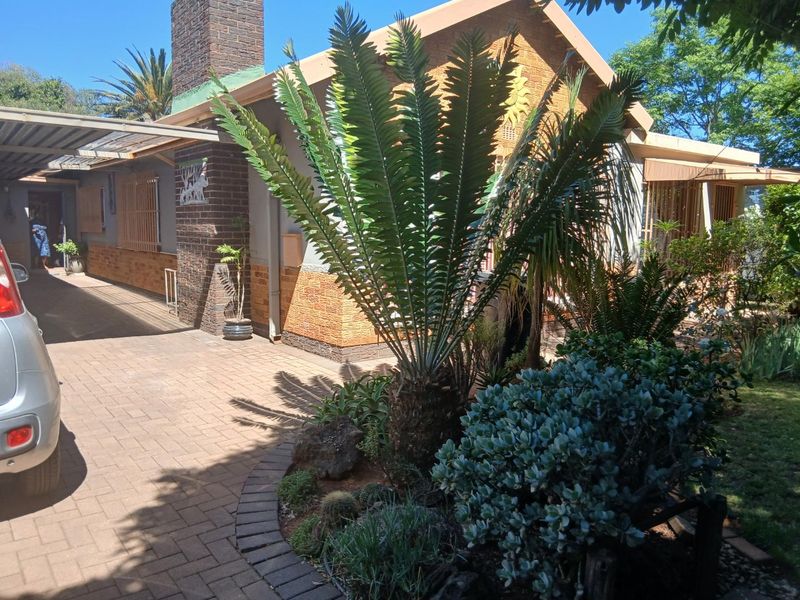 Front exterior view of the house featuring a paved driveway, carport, and brick facade with established garden landscaping.