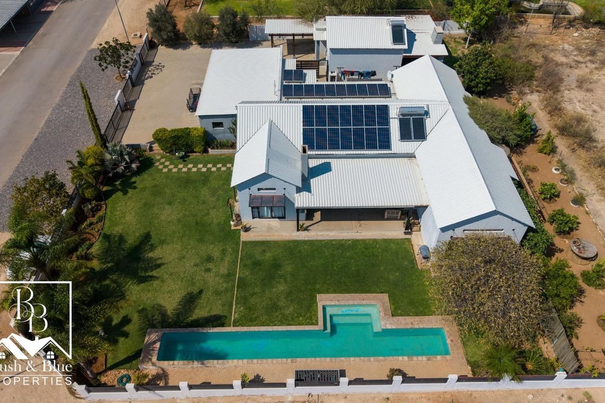 Aerial view of a residential property featuring a large swimming pool, expansive lawn, metal roofing, and integrated solar panel system.