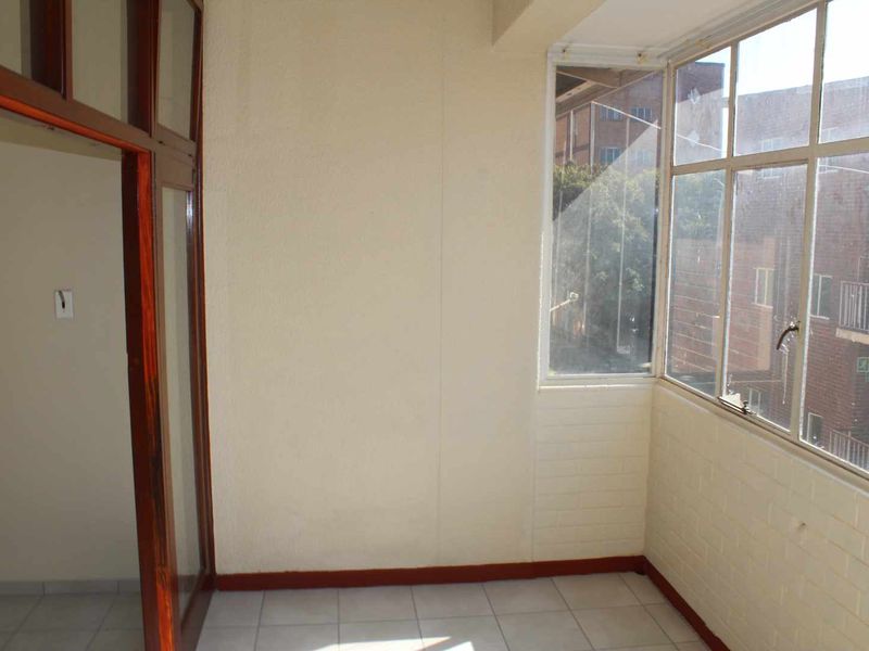 An enclosed balcony area featuring tiled flooring, large windows, and a timber door frame, offering a versatile space for potential use.