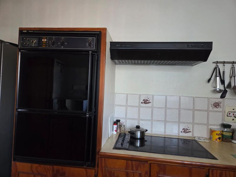 A dated kitchen area featuring a built-in double oven, ceramic hob, extractor fan, and traditional wooden cabinetry with tiled backsplash.