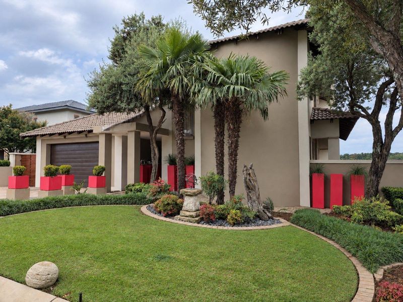 A well-maintained front elevation featuring a tiled roof, integrated garage, and manicured garden with established palm trees and paved driveway.