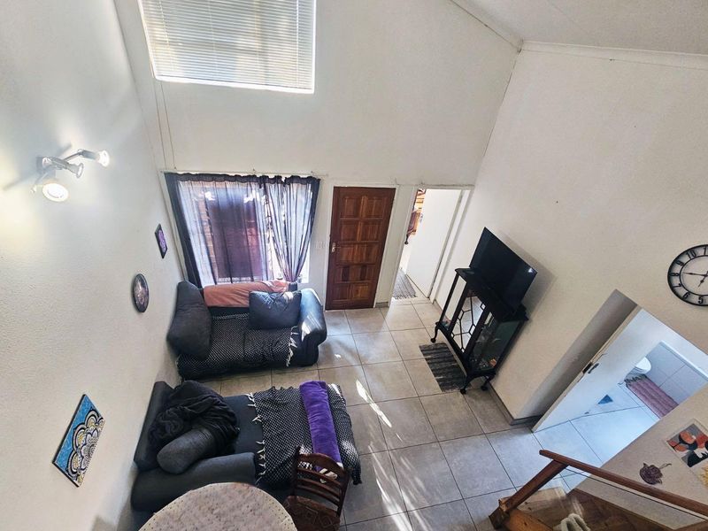 A high-ceilinged living area featuring tiled flooring, a clerestory window for natural light, and direct access to the entrance and adjacent rooms.