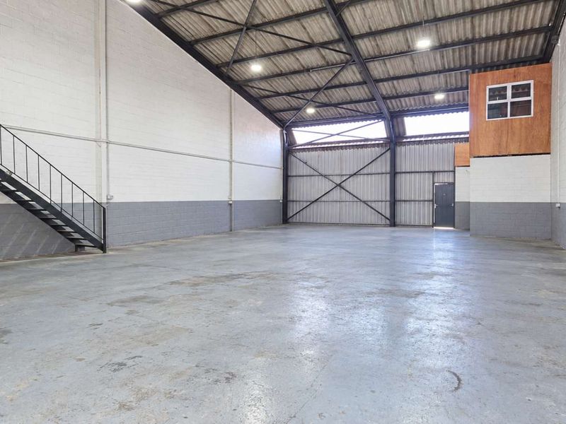 Spacious industrial warehouse unit featuring high ceilings, exposed steel trusses, a mezzanine level with staircase, and durable concrete flooring.