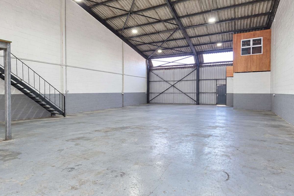 Spacious industrial warehouse unit featuring high ceilings, exposed steel trusses, a mezzanine level with staircase, and durable concrete flooring.
