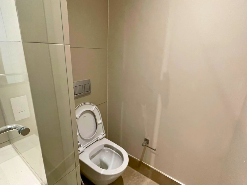 A modern bathroom featuring a wall-mounted toilet with a concealed cistern, glass shower partition, and neutral tiled finishes.