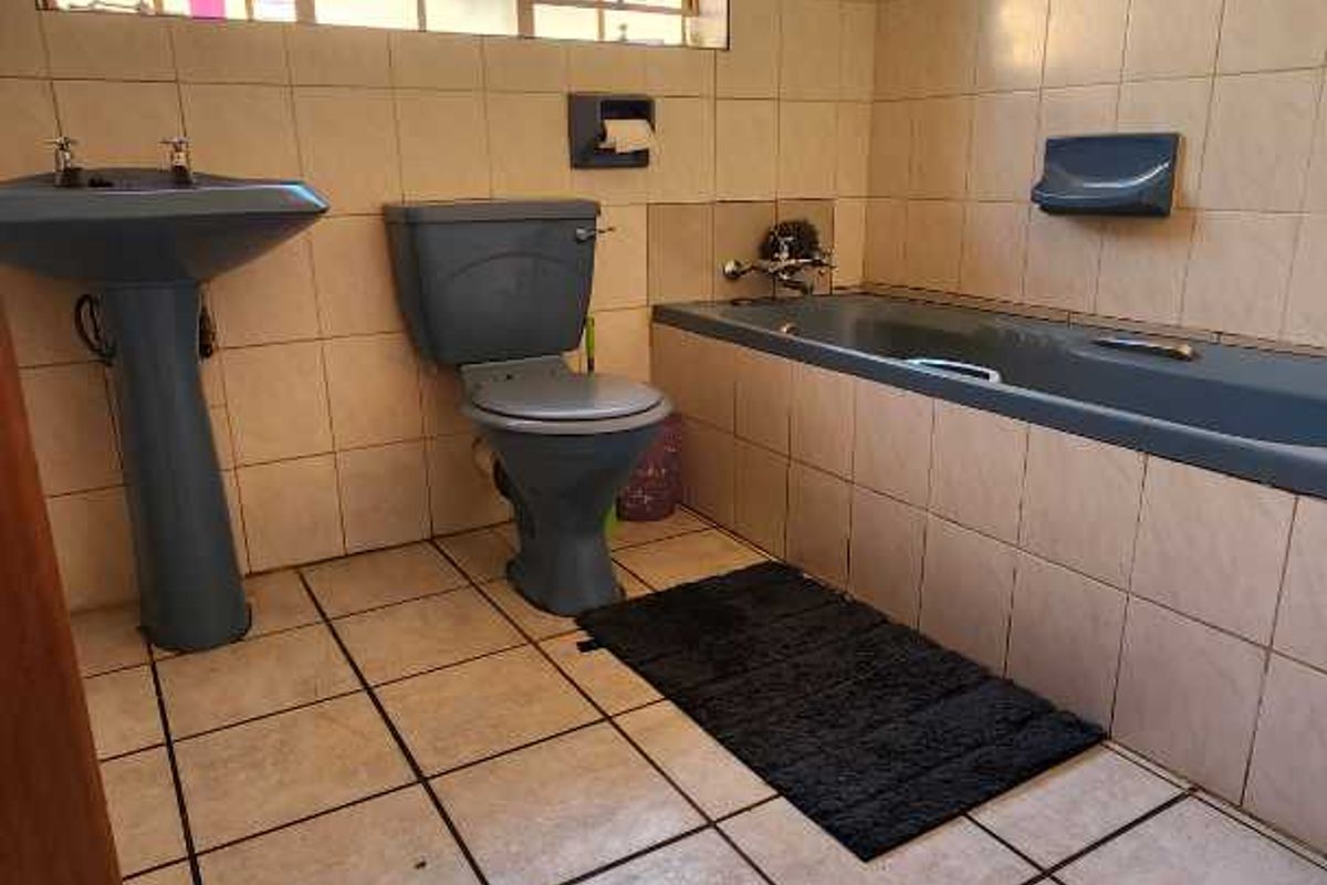 A dated bathroom featuring a grey pedestal basin, matching toilet, and built-in bathtub with full-height wall tiling and tiled flooring.