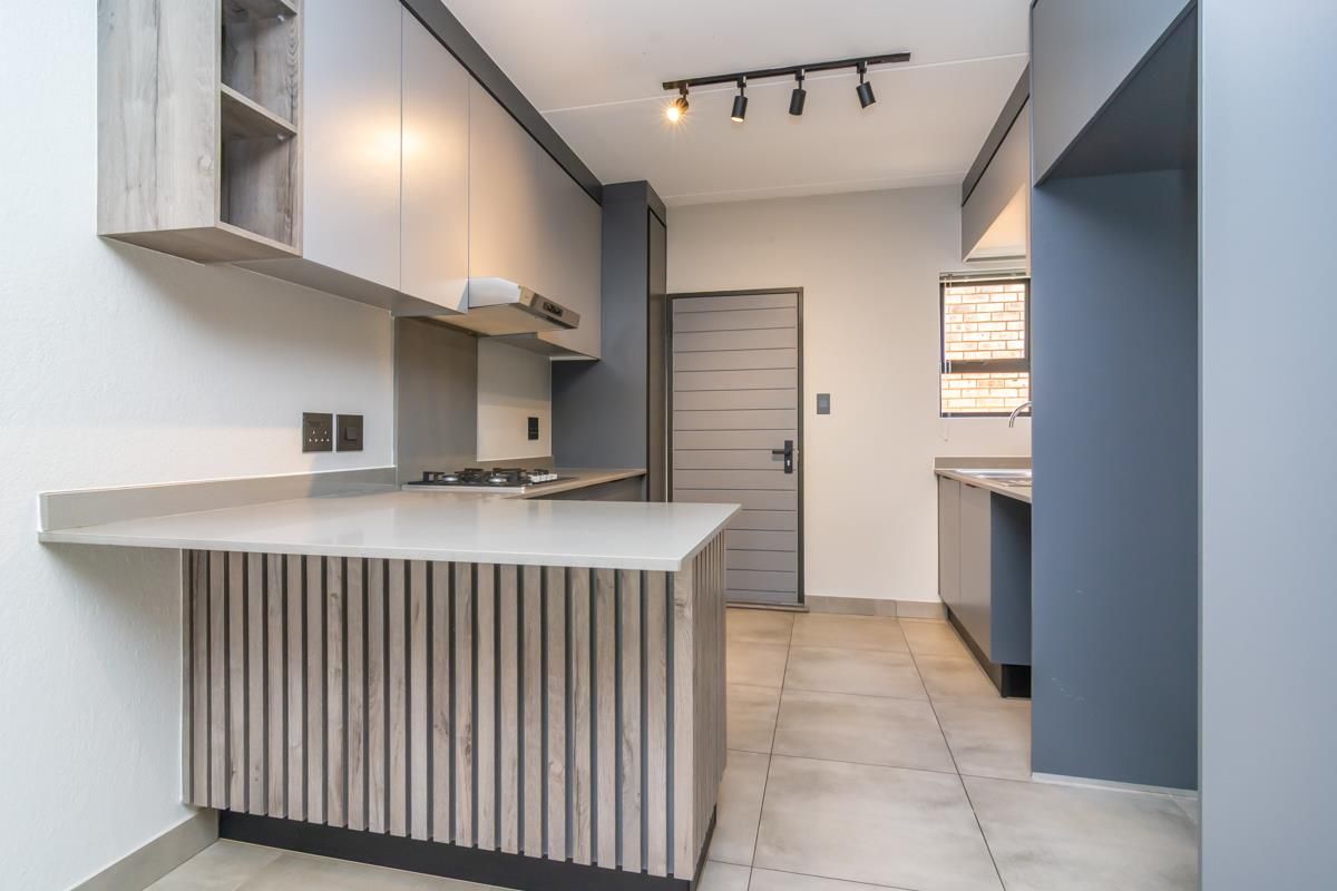 Modern kitchen featuring sleek grey cabinetry, stone countertops, a built-in gas hob, extractor fan, and contemporary track lighting.