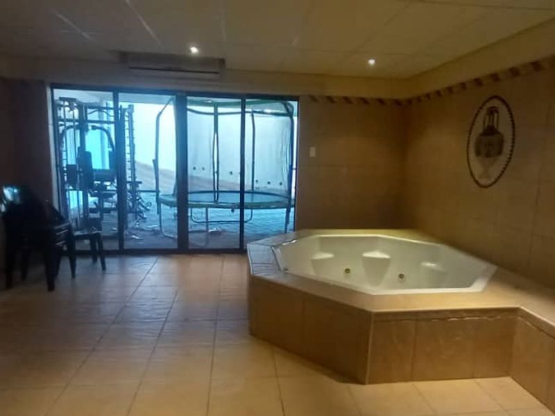 A spacious indoor gym area featuring a built-in jacuzzi, tiled flooring, and sliding glass doors leading to an outdoor space.