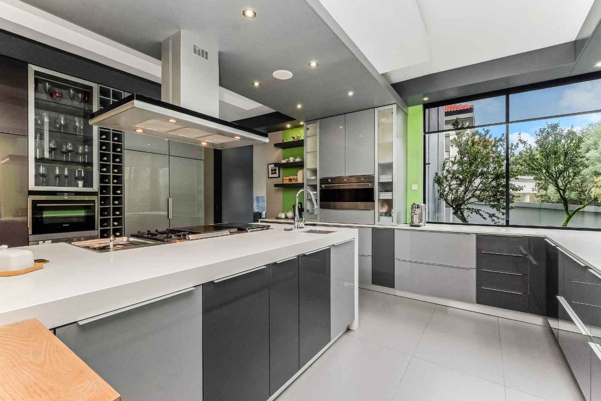 Modern kitchen featuring high-gloss cabinetry, a central island with integrated gas hob, stainless steel extractor fan, and large windows overlooking the garden.