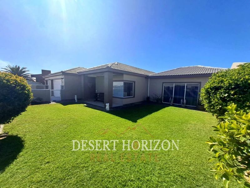 Rear view of the house featuring a well-maintained lawn, a covered patio area, and large sliding glass doors providing access to the interior.