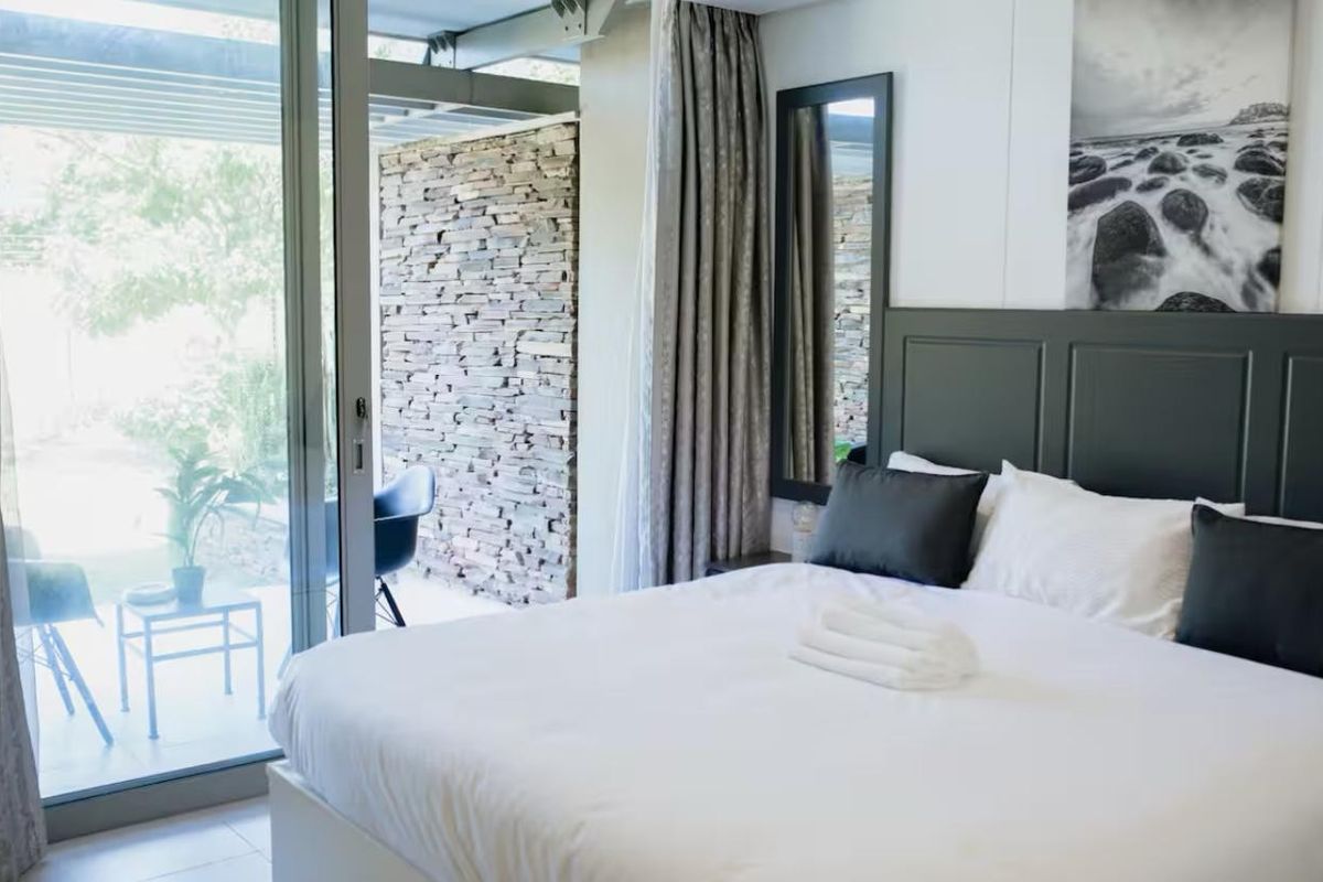 Modern bedroom featuring a built-in headboard, stone feature wall, and large sliding glass doors providing direct access to an outdoor patio area.