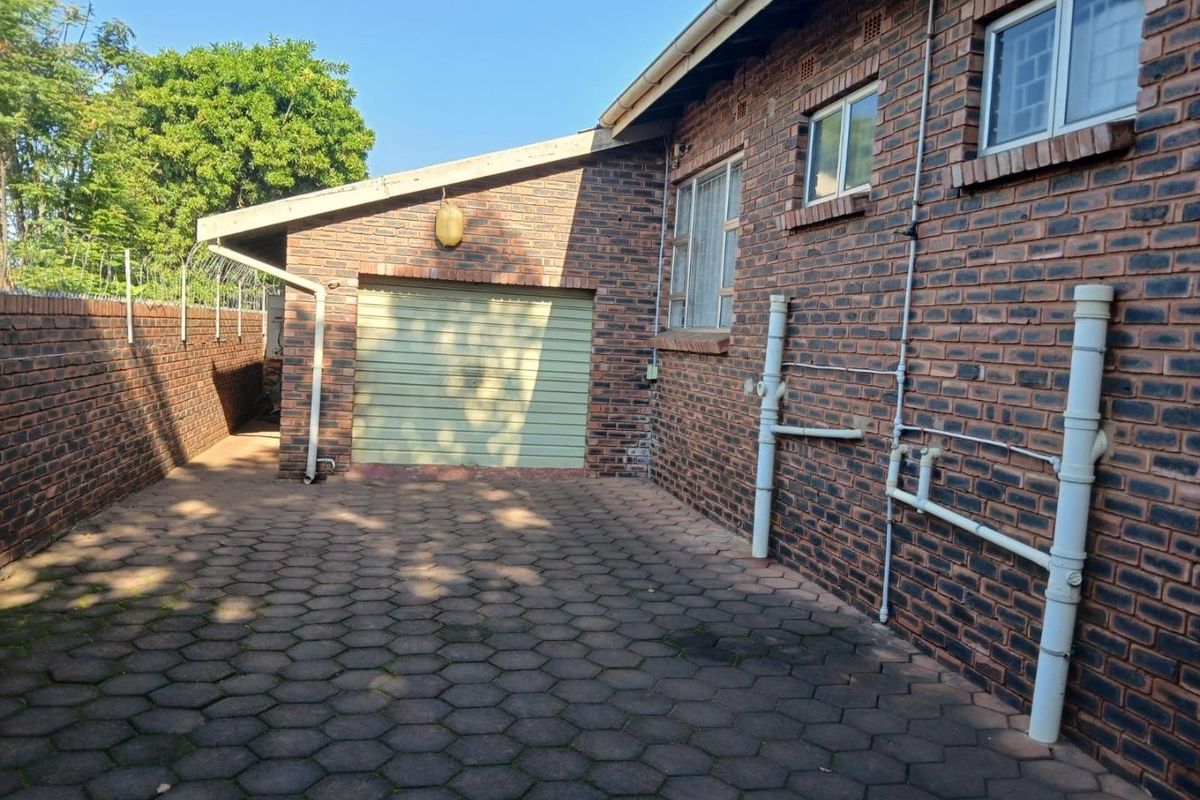 Rear exterior view of the property featuring face brick walls, a paved driveway, and a single garage door.