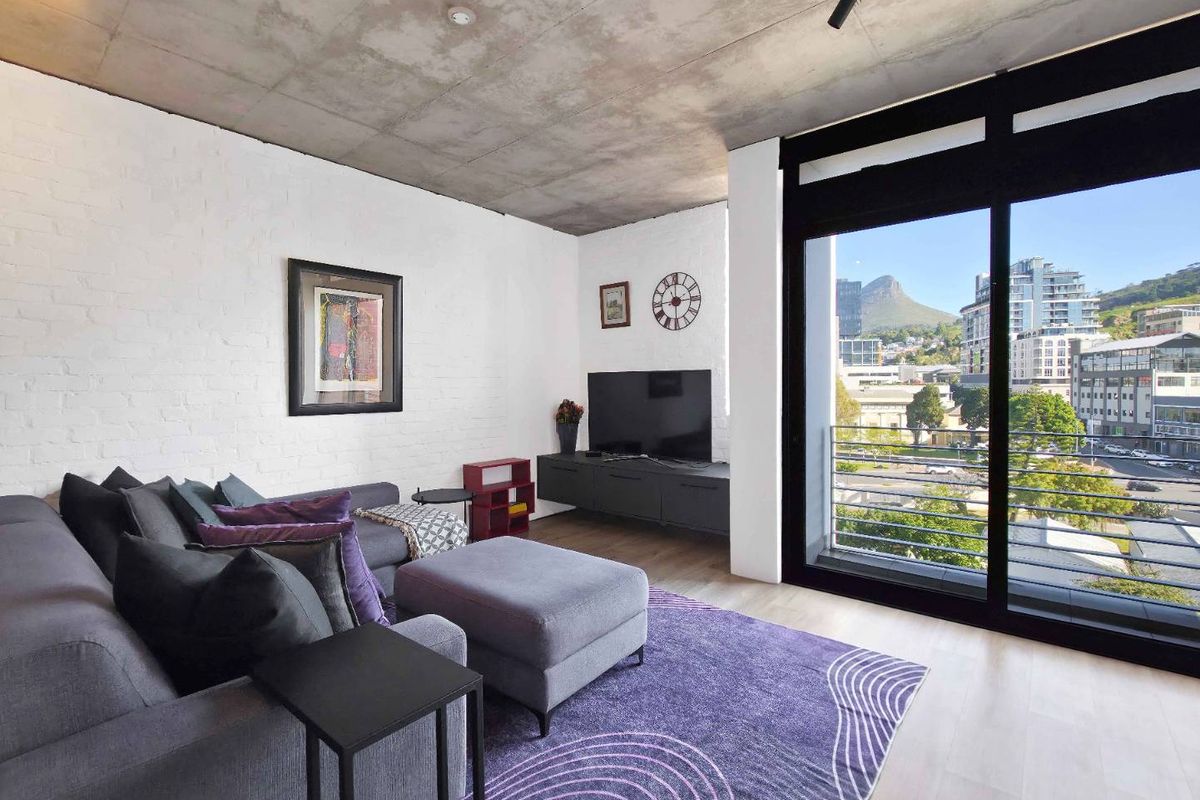 Modern living room featuring an exposed concrete ceiling, painted brick walls, and a large sliding door opening to a balcony with city views.