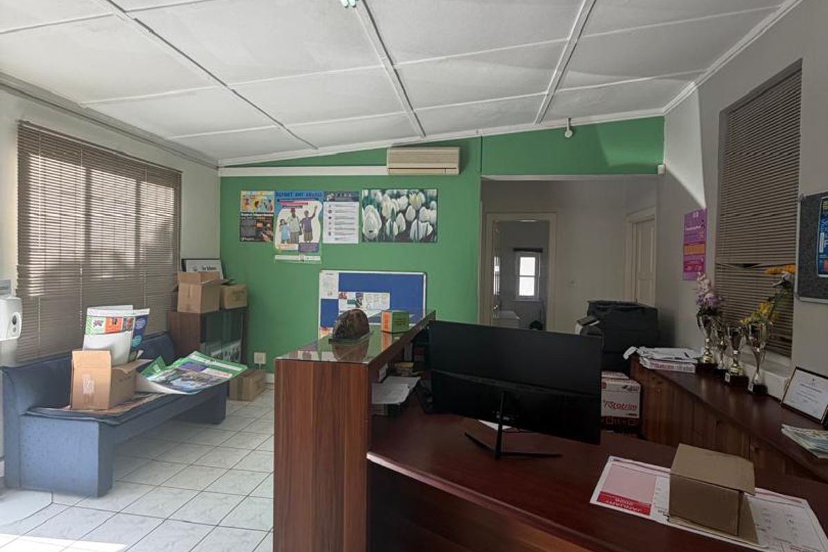 A functional office space featuring tiled flooring, a drop ceiling with integrated lighting, and a wall-mounted air conditioning unit.