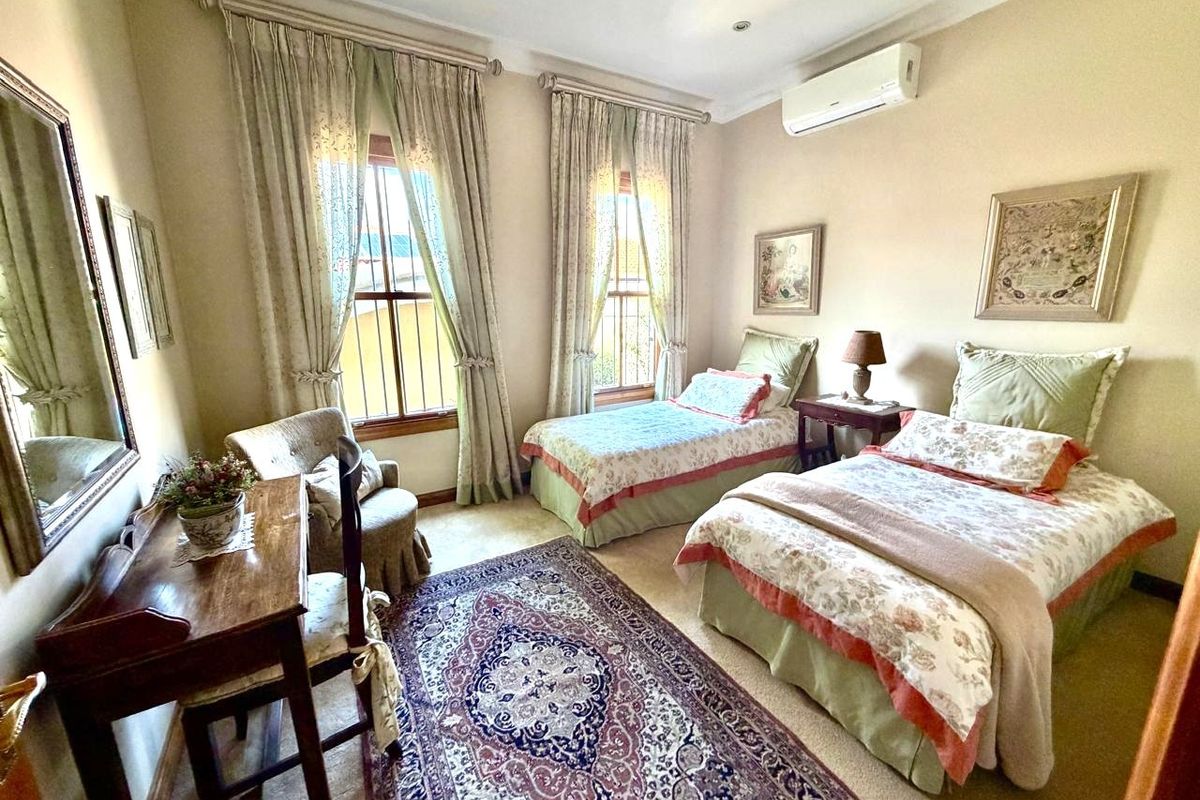 A twin bedroom featuring carpeted flooring, sash windows with curtains, and a wall-mounted split-system air conditioning unit.