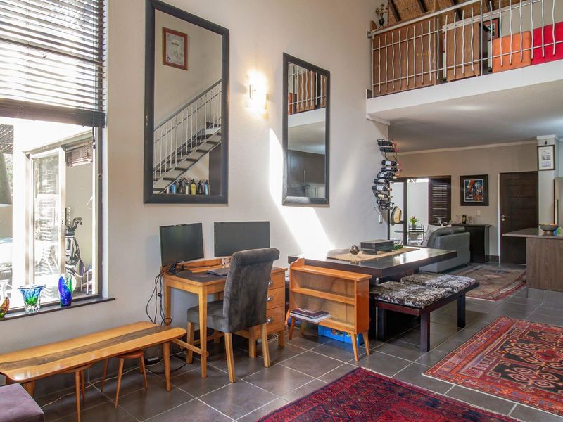 Spacious open-plan living area featuring double-volume ceilings, a mezzanine level with metal balustrades, tiled flooring, and large windows providing natural light.