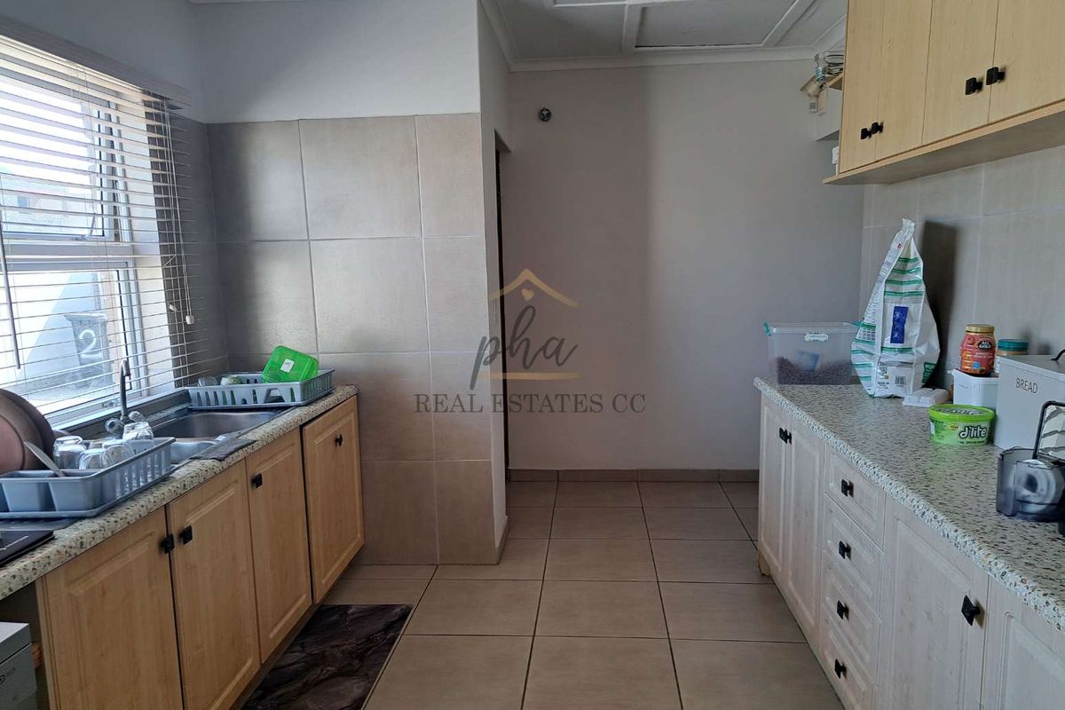 A functional kitchen featuring light wood cabinetry, granite countertops, tiled splashbacks, and tiled flooring with a window overlooking the exterior.