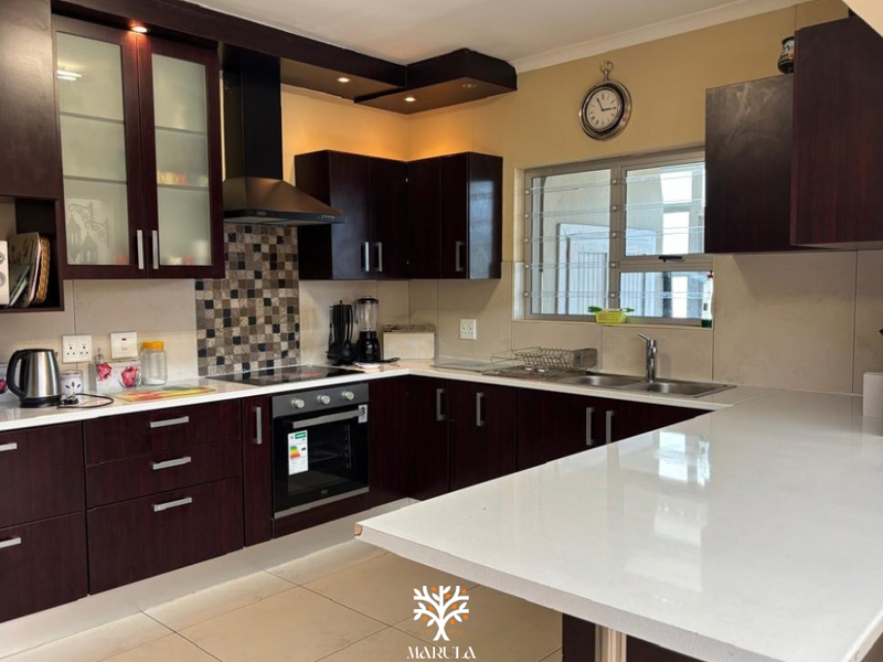 Modern kitchen featuring dark wood cabinetry, stone countertops, mosaic tile backsplash, built-in oven, and a breakfast bar peninsula.