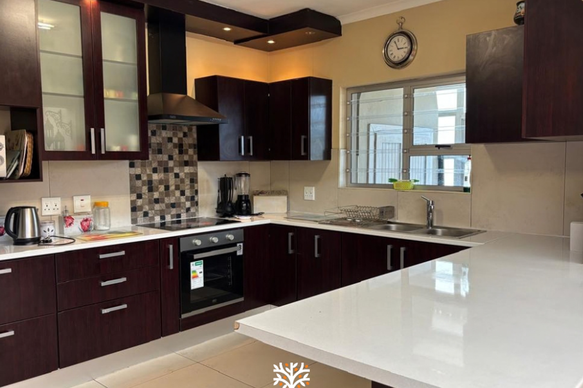 Modern kitchen featuring dark wood cabinetry, stone countertops, mosaic tile backsplash, built-in oven, and a breakfast bar peninsula.