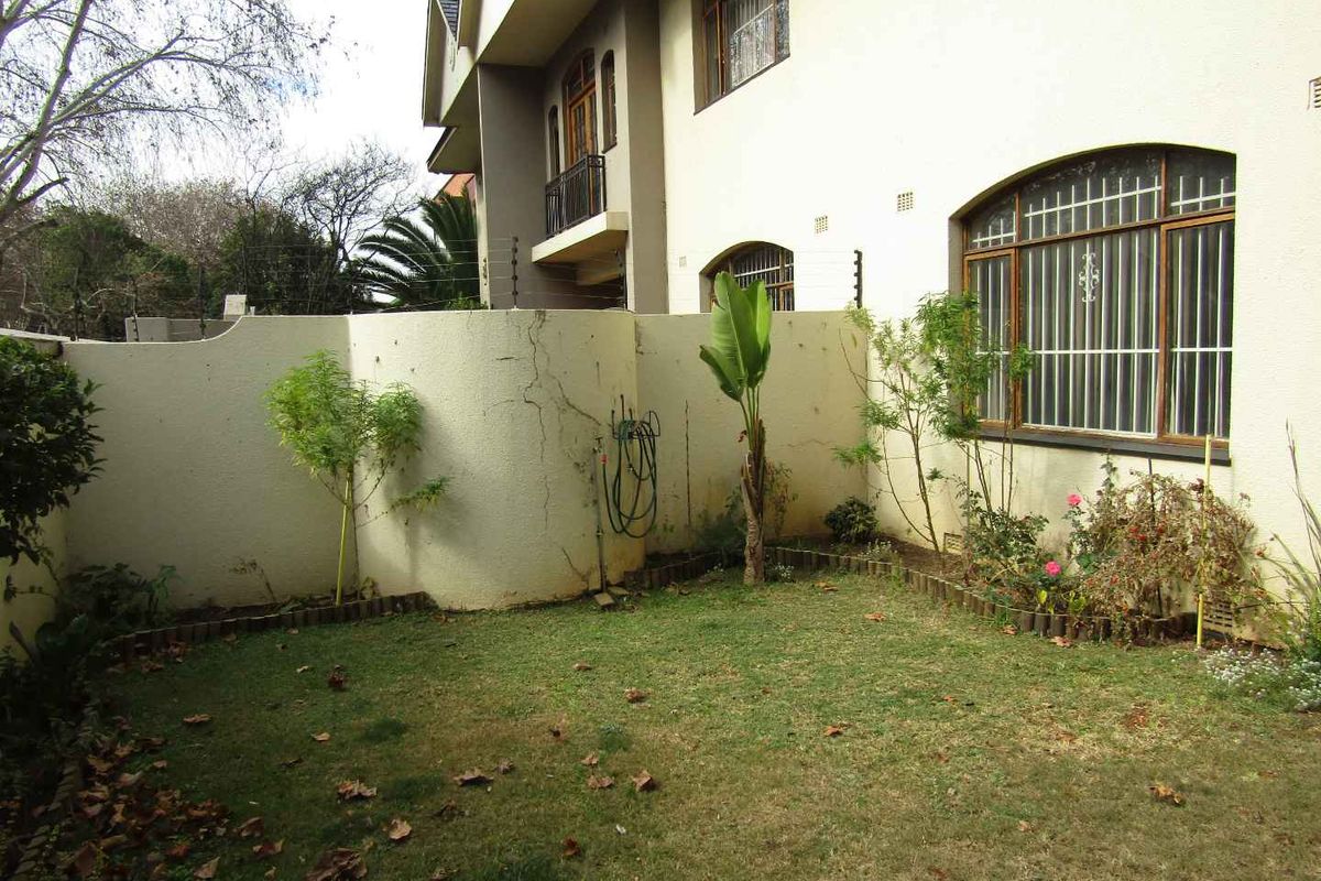 A private rear garden area featuring a lawn, established garden beds, and a boundary wall with visible structural cracking.
