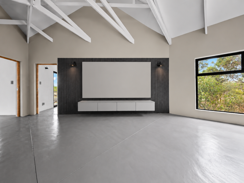 Spacious living area featuring a vaulted ceiling with exposed rafters, polished concrete floors, and a modern slatted feature wall with a floating console.
