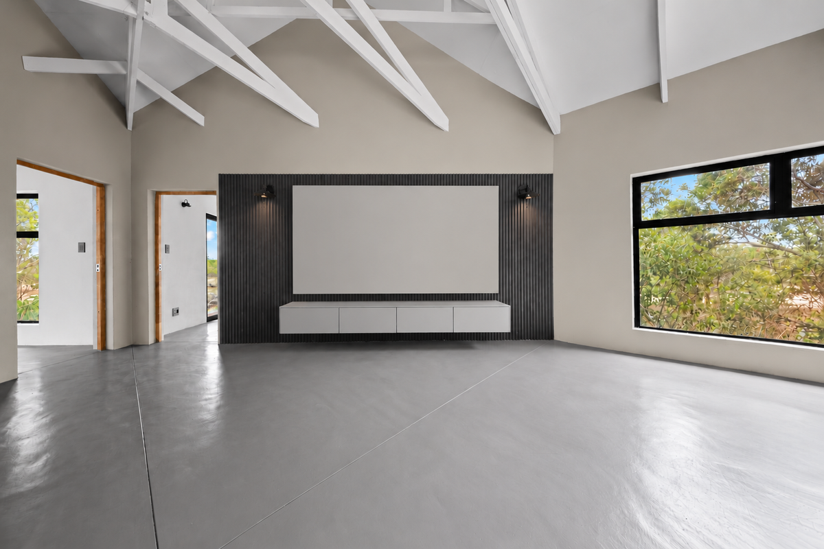 Spacious living area featuring a vaulted ceiling with exposed rafters, polished concrete floors, and a modern slatted feature wall with a floating console.