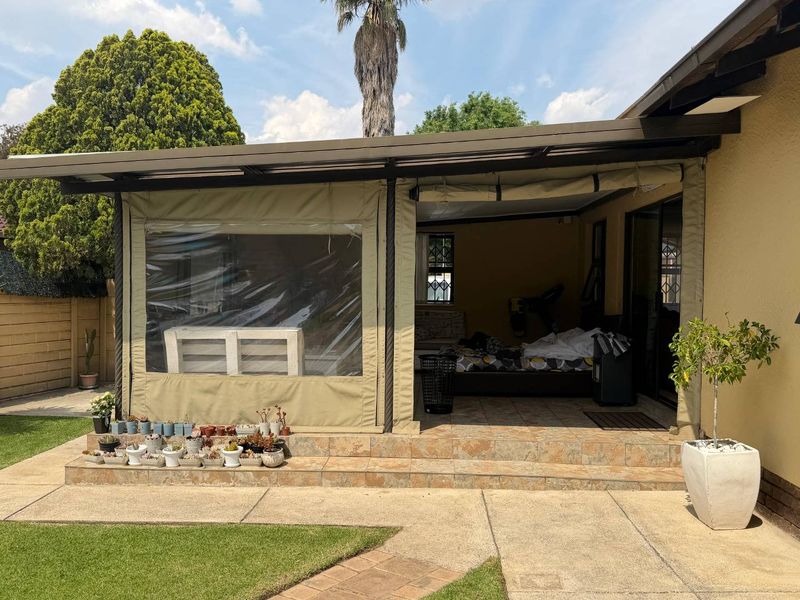 A covered outdoor patio area featuring tiled flooring and protective roll-up canvas blinds, providing a versatile space for outdoor relaxation.