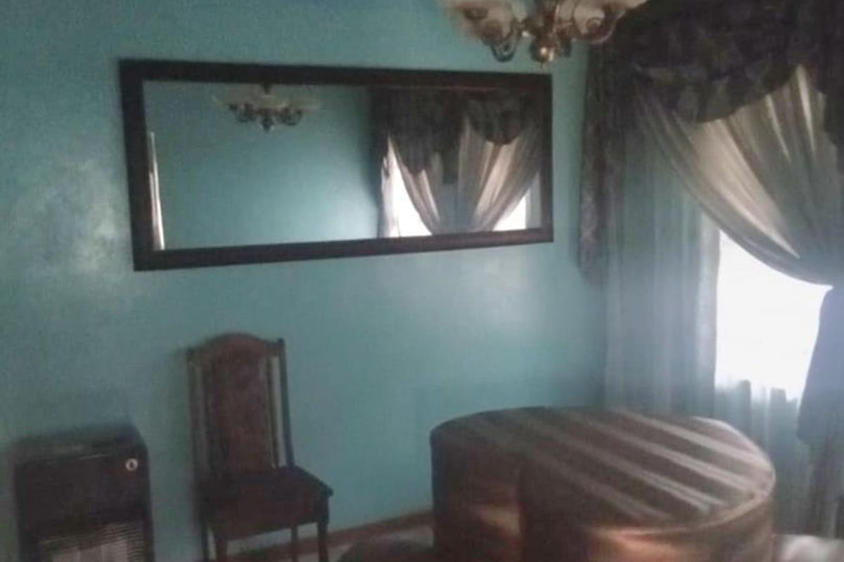 A dated living room featuring a built-in wall heater, decorative chandelier, and large wall-mounted mirror.
