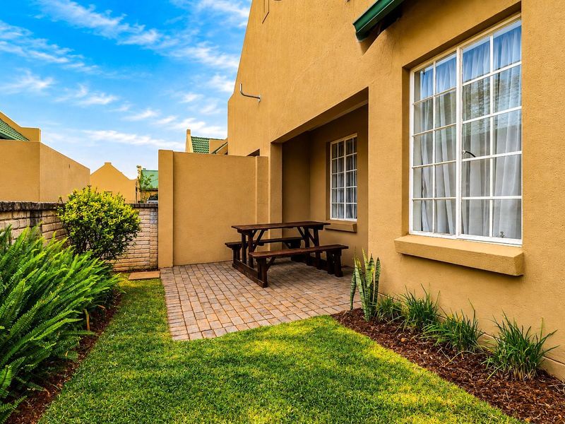 A private rear garden featuring a paved patio area, well-maintained lawn, and brick boundary wall, providing a pleasant outdoor space for the townhouse.