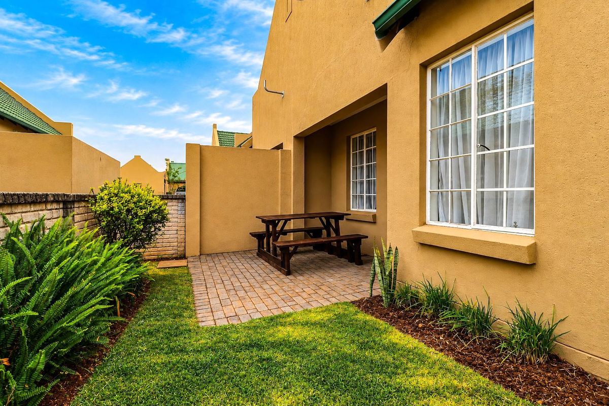 A private rear garden featuring a paved patio area, well-maintained lawn, and brick boundary wall, providing a pleasant outdoor space for the townhouse.
