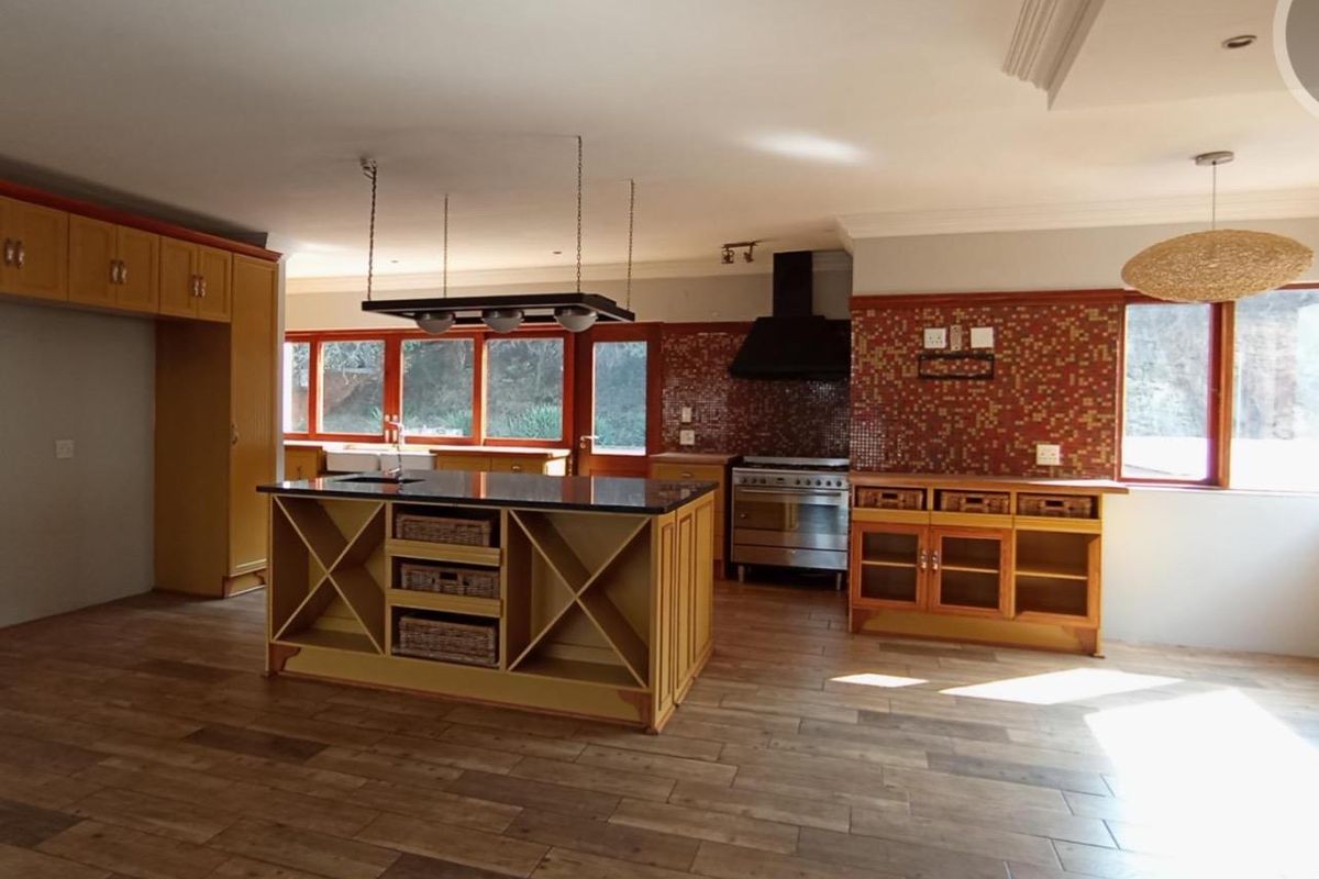 Spacious kitchen featuring a central island, gas stove with extractor, tiled splashback, and ample built-in cabinetry with timber-look flooring.