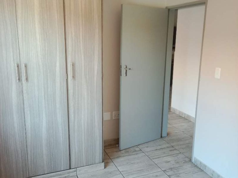 A clean, empty bedroom featuring light wood-grain built-in cupboards and neutral tiled flooring, providing a versatile space ready for personalization.