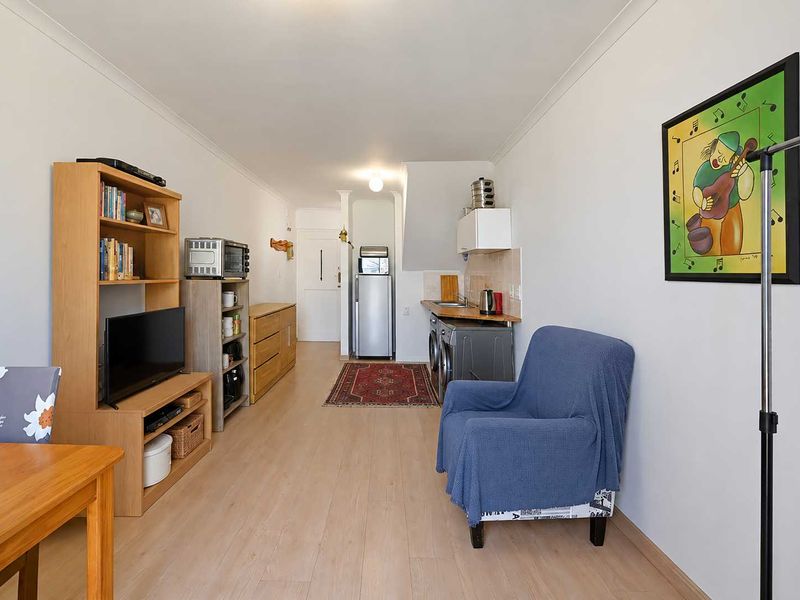 Open-plan living area featuring light laminate flooring and a compact kitchenette with built-in cabinetry and tiled splashback.