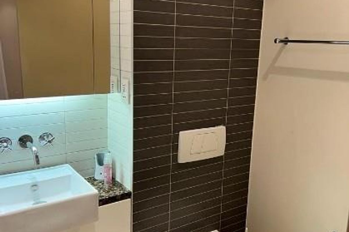Modern bathroom featuring a wall-mounted toilet, a sleek vanity with a basin, and dark tiled accent wall.