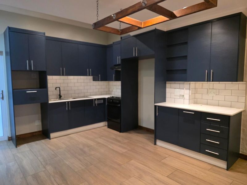 Modern kitchen featuring navy blue cabinetry, white subway tile backsplash, stone countertops, and a unique timber ceiling feature with wood-look tile flooring.