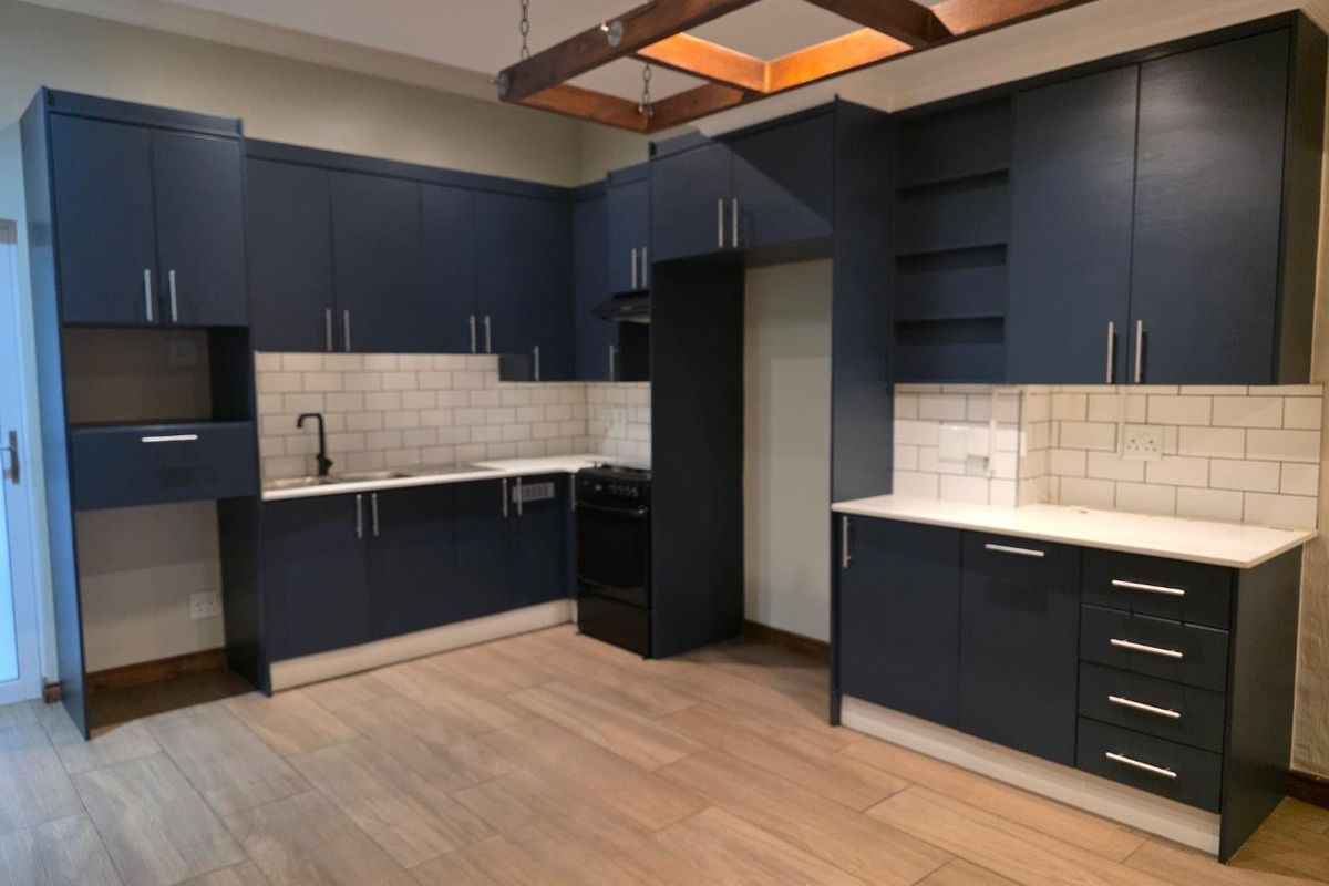 Modern kitchen featuring navy blue cabinetry, white subway tile backsplash, stone countertops, and a unique timber ceiling feature with wood-look tile flooring.