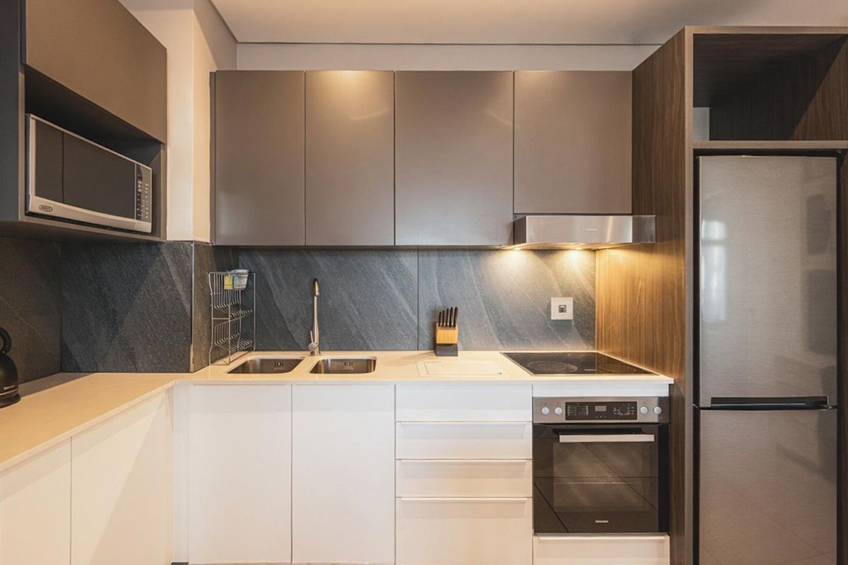 Modern kitchen featuring sleek cabinetry, stone backsplash, integrated appliances including an oven, hob, and microwave, providing a clean and functional culinary space.
