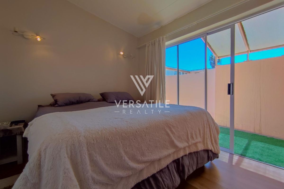 A comfortable bedroom featuring laminate flooring, wall-mounted lighting, and a large sliding glass door providing direct access to an outdoor patio area.