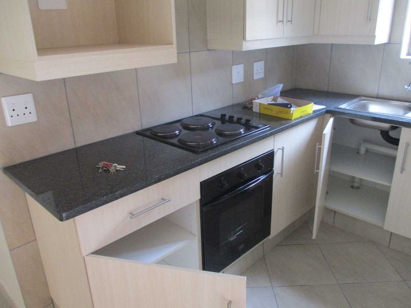A functional kitchen featuring light wood cabinetry, dark granite countertops, a built-in electric oven and hob, and neutral tiled flooring.