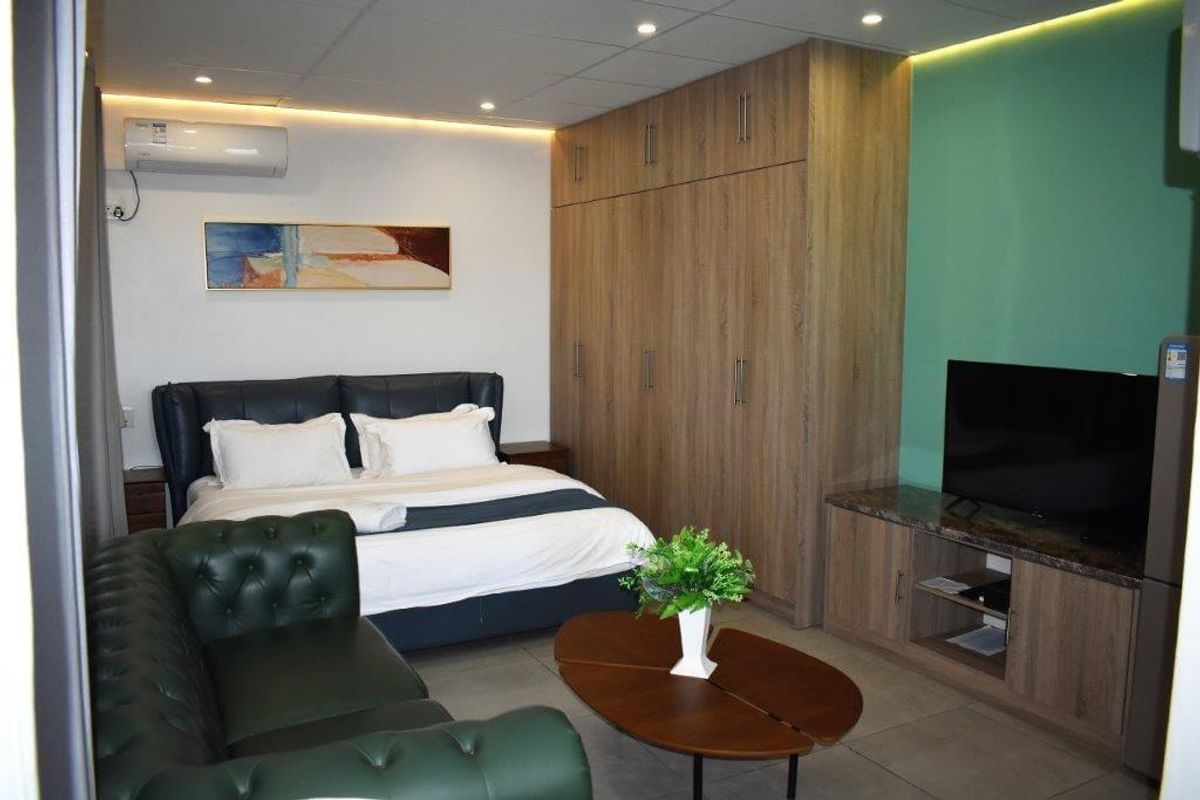 A well-appointed hotel bedroom featuring built-in wooden cabinetry, integrated air conditioning, and modern recessed ceiling lighting.