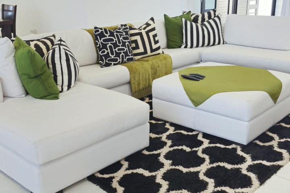 A bright and modern living room featuring large white floor tiles, recessed ceiling lighting, and access to the outdoors through glass-paned french doors.
