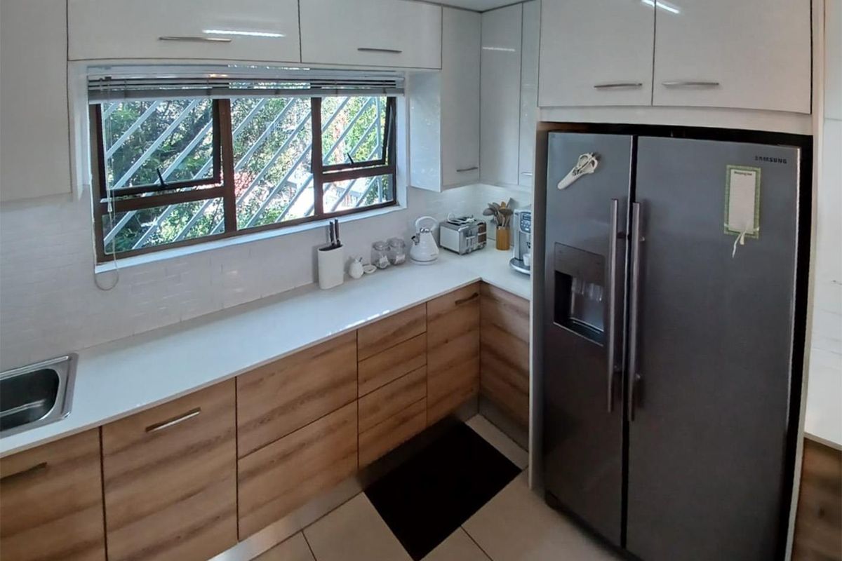 A modern kitchen featuring light wood-grain cabinetry, white upper cabinets, white countertops, a stainless steel sink, and a large double-door refrigerator.