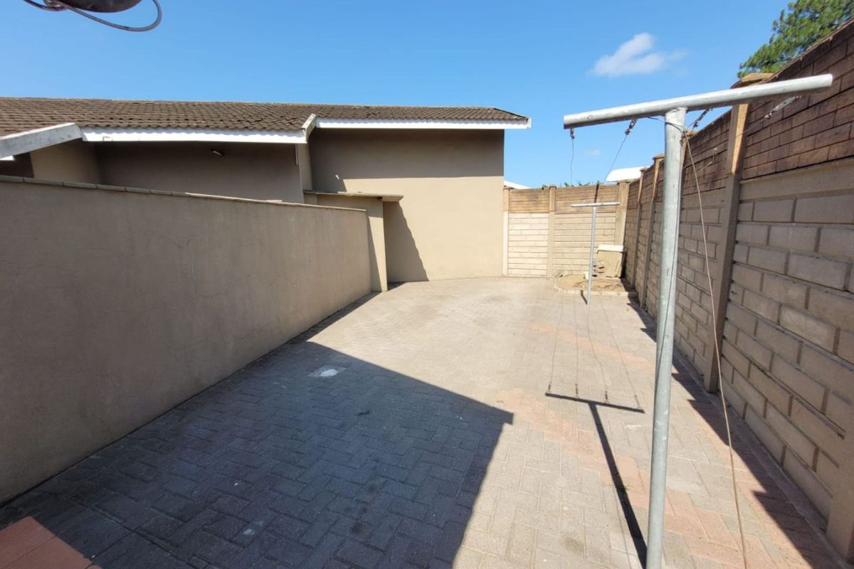 A private paved rear courtyard area featuring high perimeter boundary walls and a fixed metal washing line structure.