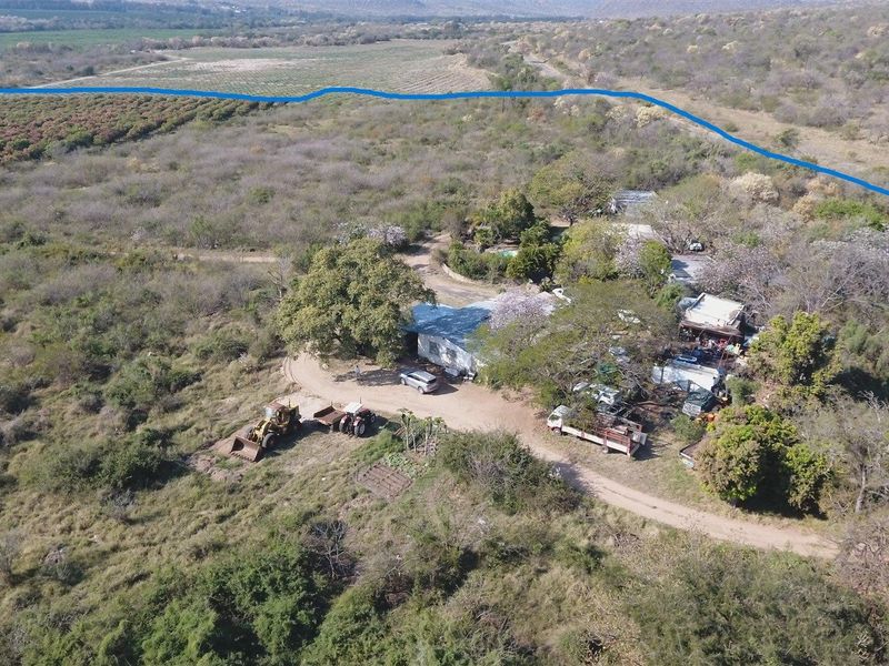 Aerial view of a rural farm property featuring a main dwelling, surrounding outbuildings, and extensive natural landscape with established trees and access tracks.