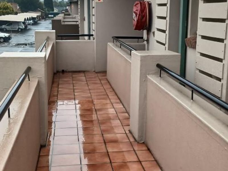 An outdoor balcony area featuring tiled flooring, a metal balustrade, and a wall-mounted fire hose reel.