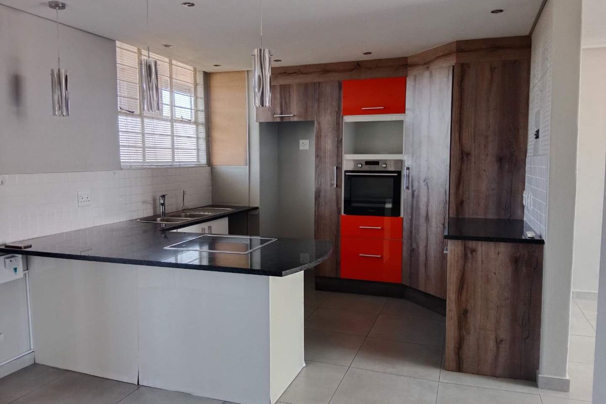 Modern kitchen featuring granite countertops, built-in oven, hob, double sink, and a combination of wood-look and vibrant orange cabinetry with tiled flooring.