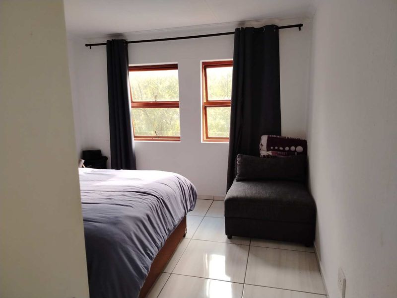 A bedroom featuring tiled flooring and timber-framed windows with dark curtains.