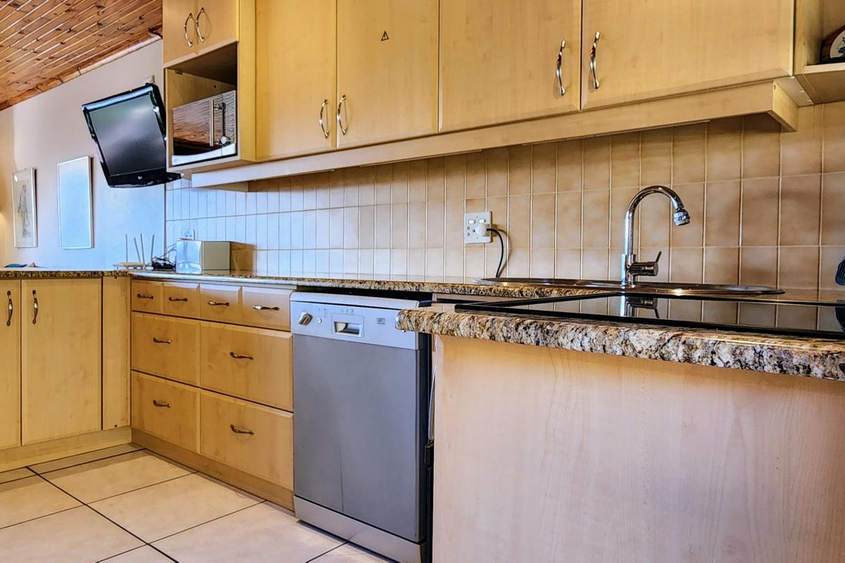 A functional kitchen featuring light wood cabinetry, granite countertops, tiled backsplash, and integrated dishwasher.