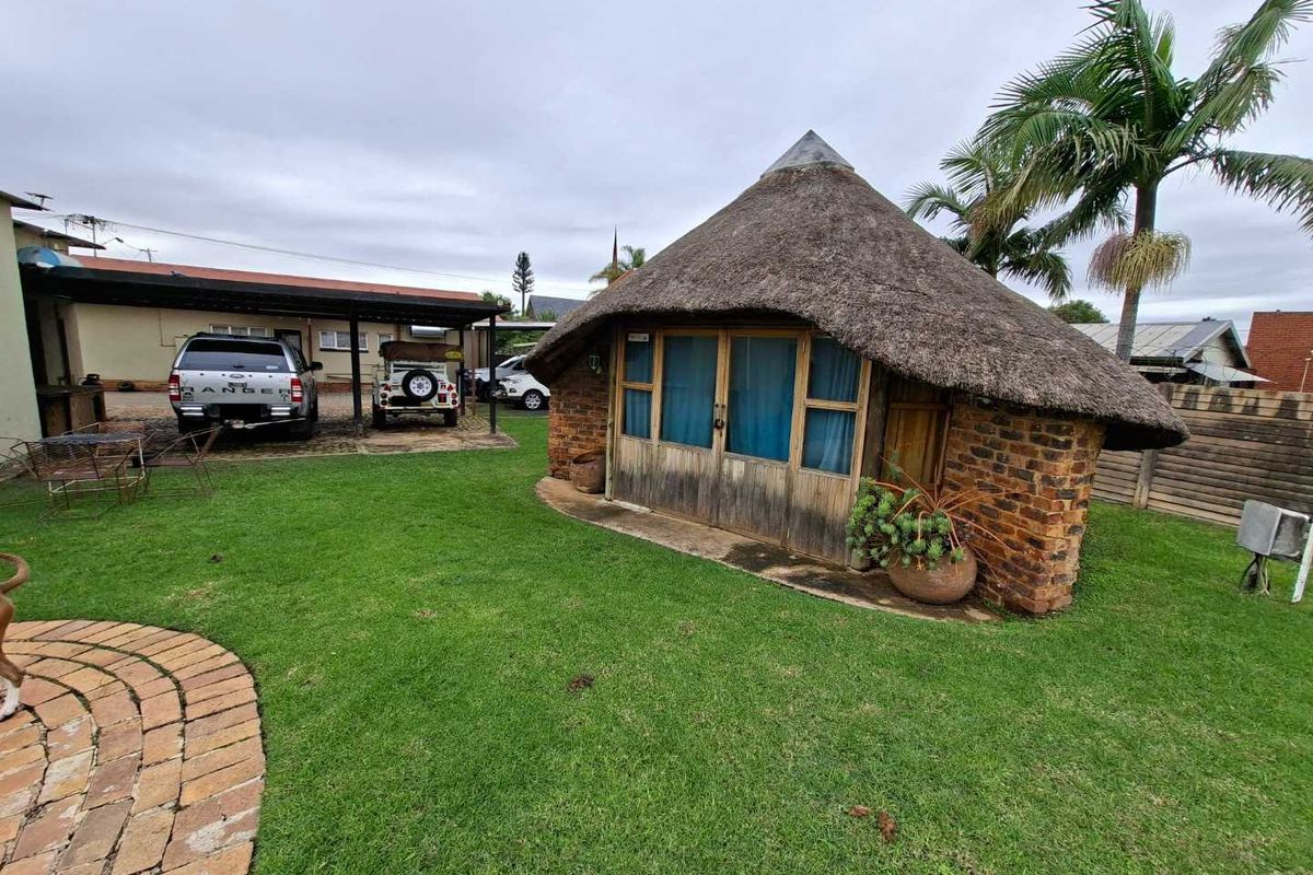 A detached garden structure featuring a traditional thatched roof and brick exterior, situated in a well-maintained lawn area with an adjacent carport.