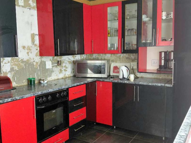 A kitchen featuring high-contrast red and black cabinetry, dark tiled flooring, and a built-in oven, currently requiring wall surface repairs and splashback installation.